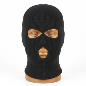 Pasamontaña negro de punto de tres agujeros (dos ojos y boca) colocado sobre un busto de madera, que muestra en detalle su textura de lana tejida fina y sus orificios con costuras reforzadas de la tienda Disfraces Lucero.