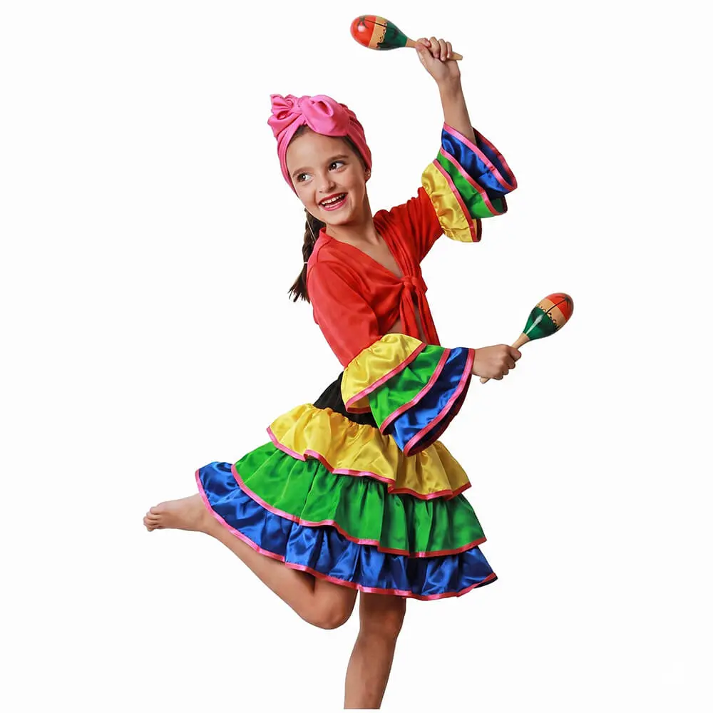 Niña sonriendo de frente sosteniendo dos maracas de juguete luciendo el disfraz de brasileña infantil de tres piezas con camisa de volantes, falda multicolor satinada y pañuelo rosa en la cabeza de la tienda Disfraces Lucero.